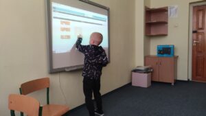 Chłopiec - uczestnik zajęć kółka rozwijającego zainteresowania informatyczne rozwiązuje zadanie dotyczące kodowania na tablicy interaktywnej.