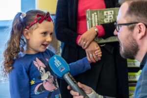 dziewczynka w niebieskiej bluzce udziela wywiadu reporterowi z mikrofonem