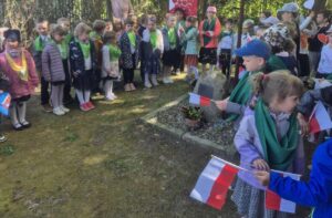 Zdjęcie przedstawia przedszkolaki ubrane w stroje galowe trzymające w dłoniach biało-czerwone flagi.