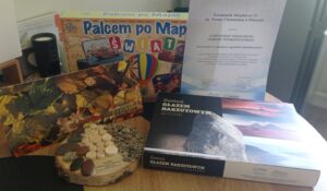 na zdjęciu gry edukacyjne o tematyce przyrodniczej, papierowy certyfikat oraz drewniana statuetka przypominająca ścieżkę sensoryczną.