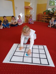 Na pierwszym planie zdjęcia widać dziewczynkę przesuwającą kropkę na kratkowanej planszy.