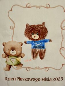 Na fotografii widać pracę plastyczną dziecka przedstawiającą brązowego pluszowego misia w niebieskim sweterku. Rysunek znajduje się w fantazyjnej ramce z postacią pluszowego misia