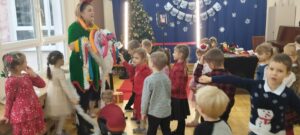 Na zdjęciu widać grupę dzieci, które przebierają Elfa za choinkę, nakładając na niego różnorodne łańcuchy, bombki, ozdoby.